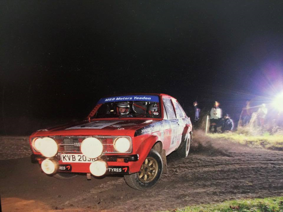 A red classic rally car with M&D Motors Yeadon lettering on its windscreen